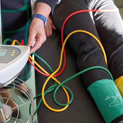 Medical professional performing a vascular test on a patient's leg with colorful tubes and cuffs.